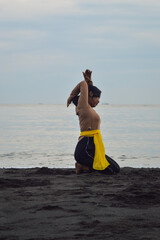 A single teen girl practices yoga while sitting on her heels, her right arm elegantly raised above...