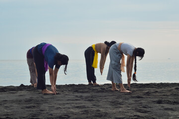 Bending deeply, all girls reach their arms down past their right legs in a focused stretch,...
