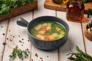 Hot salmon soup with herbs and vegetables in dark bowl on rustic table