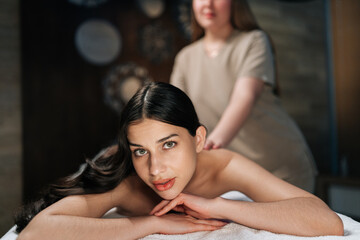 Portrait of attractive young woman looking at camera, lying on massage table during professional...