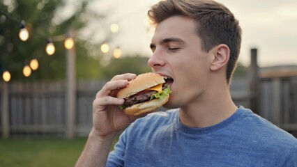 Young man enjoying a juicy burger outdoors at sunset