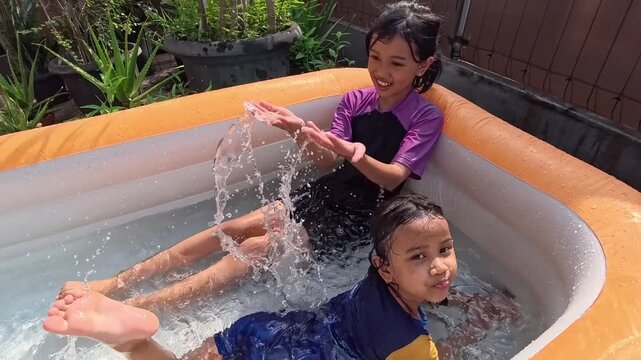Two Asian sisters playing water in an inflatable pool in the backyard