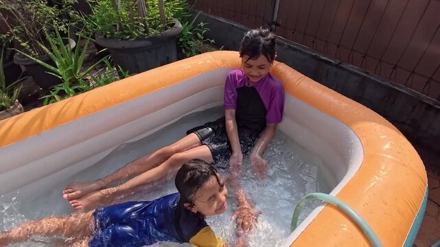 Two happy little Asian girls playing water in an inflatable pool in the backyard