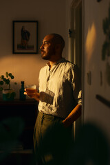 Man with a drink indoors in warm evening light. 