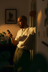 Man using cellphone indoors in warm evening light. 