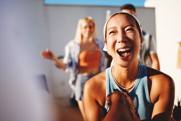 Excited young woman shaking hand and laughing with friend at a rooftop party