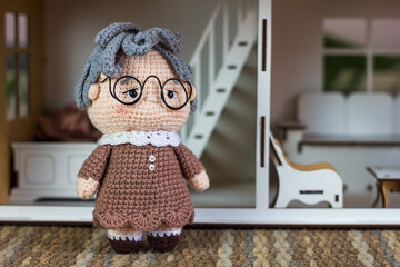 Crochet amigurumi granny toy near doll house on lawn, own home in retirement