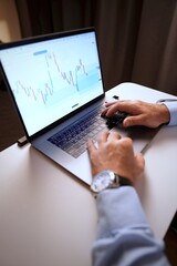 Close-up of man’s hands on laptop keyboard, trading chart on screen. Concept of online work, analytics, investing, finance, market strategy, cryptocurrency.
