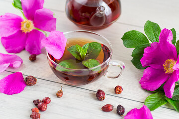 Healing rosehip and mint tea in cup and teapot from above on light wooden table