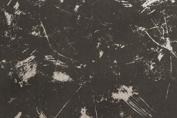 A dark, textured surface shows a chaotic pattern of light-colored scratcht and debris scattered...