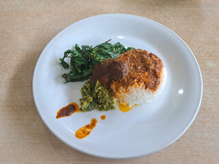 A plate of Padang cuisine, cassava leaves, curry sauce, and green chili sauce