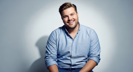 Cheerful plus-size man in light blue button-down shirt laughing against gray studio background. Body positivity, confidence, diversity concept.