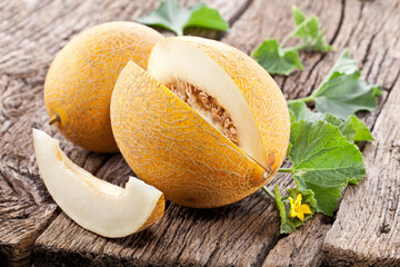 Galia melons with green leaves on wooden table.