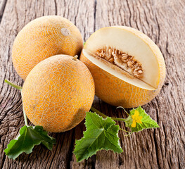 Galia melons with green leaves on wooden table.