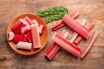 Cuts of red rhubarb stem on wooden plate on the table, top view.