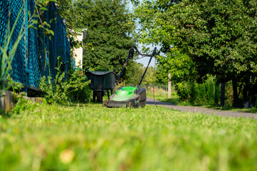 A person mows the grass in a peaceful residential area surrounded by trees and greenery on a clear,...