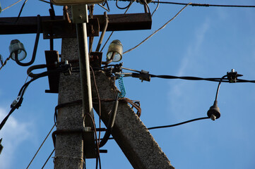 Electrical infrastructure shows power lines and utility attachments against a clear blue sky with a...