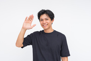 A friendly young Asian man smiling warmly while waving with one hand. Isolated on a white...