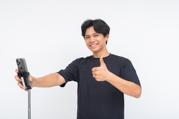 A happy young Asian man flashing a thumbs up and smiling proudly, holding a phone mounted on a...