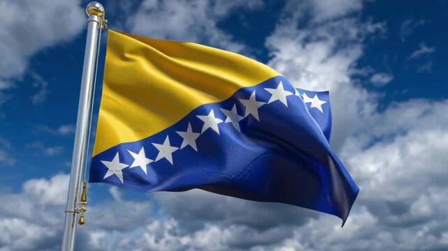 The flag of Bosnia  Herzegovina waves against a cloudy blue sky attached to a silver flagpole