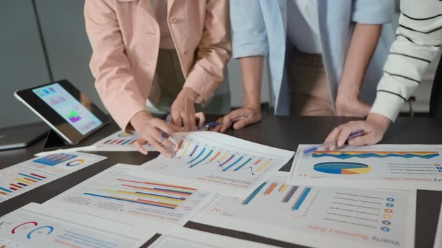 Close-up of asian coworkers pointing at printed charts during a business meeting, analyzing graphs and performance metrics to support a data-driven decision and promote smart data-driven decision maki