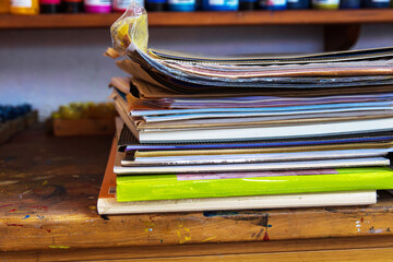 A colorful stack of sketchbooks, drawing pads, paper portfolios,  layers of paper, canvas boards,...