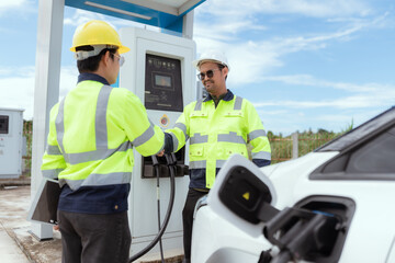 Technicians interacting at an electric vehicle charging station during daylight hours in a modern...