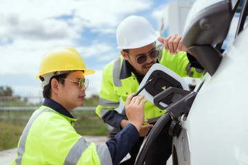 Two technicians inspect electric vehicle charging station in bright daylight while discussing details of the charging process