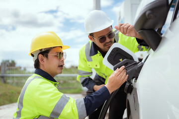 Two technicians inspect electric vehicle charging station in bright daylight while discussing details of the charging process