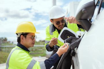 Two technicians inspect electric vehicle charging station in bright daylight while discussing details of the charging process