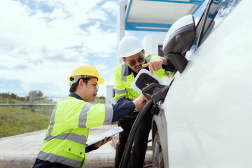 Two technicians inspect electric vehicle charging station in bright daylight while discussing details of the charging process
