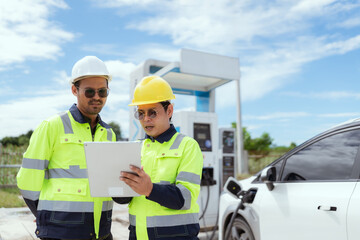 Electric vehicle charging experts discuss project details at a modern charging station in bright daylight