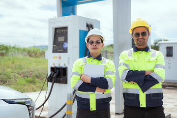 Two workers at a charging station smile and promote electric vehicle adoption in a rural area during daylight