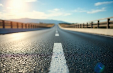 Empty asphalt road stretching into the distance under a bright blue sky with clouds and mountains in the background