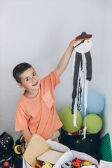 Smiling little boy proudly shows his handmade pirate craft in a cozy playroom, surrounded by toys...