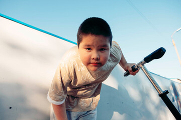Asian teen boy looking into camera while holding scooter low angle portrait with direct gaze