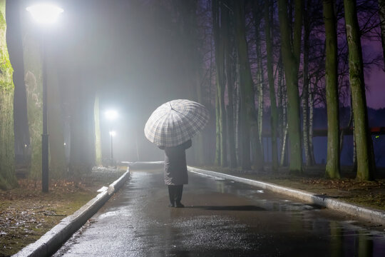 A woman walks late at night in a foggy park