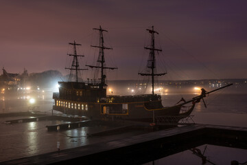 On a winter night, an ancient frigate stands frozen in ice at the pier