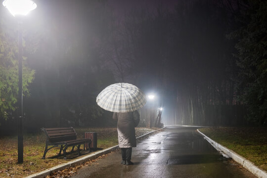 A woman walks late at night in a foggy park