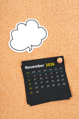 November 2026 Black calendar page and blank speech bubble with thumbtack on wooden board.