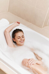 Relaxed young woman enjoying a bubble bath, smiling and unwinding in the tub, surrounded by soft...