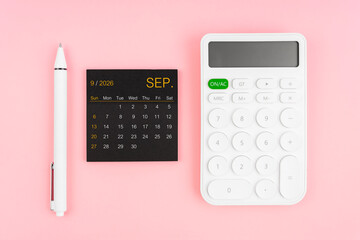 September 2026 calendar and white calculator with pen on pink color background.