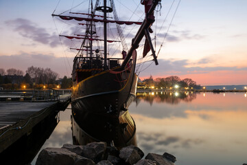 On a spring evening at sunset, an ancient frigate with scarlet sails stands frozen in time at the pier