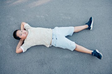 Mindful rest outdoors Calm child, Asian teen boy lying with arms behind head on street