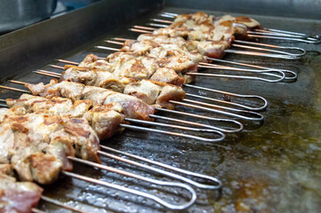 Delicious skewers of marinated meat are grilling on a hot surface in a vibrant street food market...