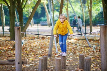 Obraz premium Cheerful little girl having fun on playground in autumn park in Paris, France.