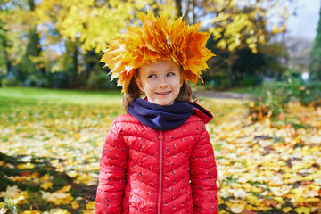 Adorable preschooler girl in maple leaves head decoration enjoying nice and sunny autumn day outdoors. Happy child walking on a fall day in Paris, France.