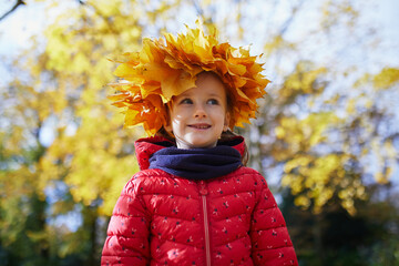 Adorable preschooler girl in maple leaves head decoration enjoying nice and sunny autumn day outdoors. Happy child walking on a fall day in Paris, France.