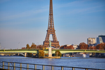 Eiffel tower over the river Seine with Grenelle bridge and Statue of Liberty on a bright fall day in Paris, France.