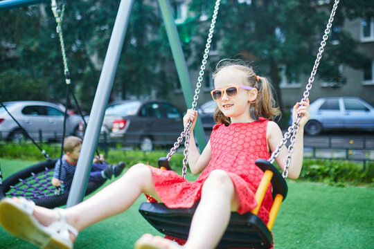 Happy 6 years old girl on a swing. Happy kid on playground swinging on seesaw. Outdoor summer activities for children.